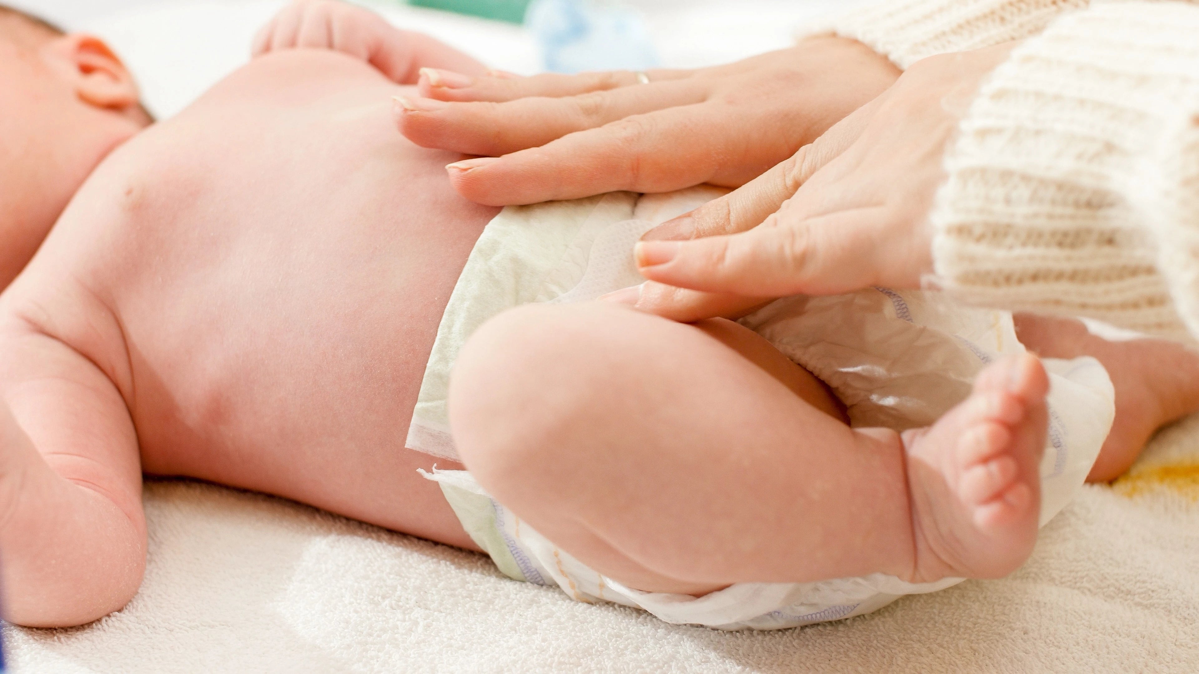 Baby in a diaper with a hand adjusting it on a light background
