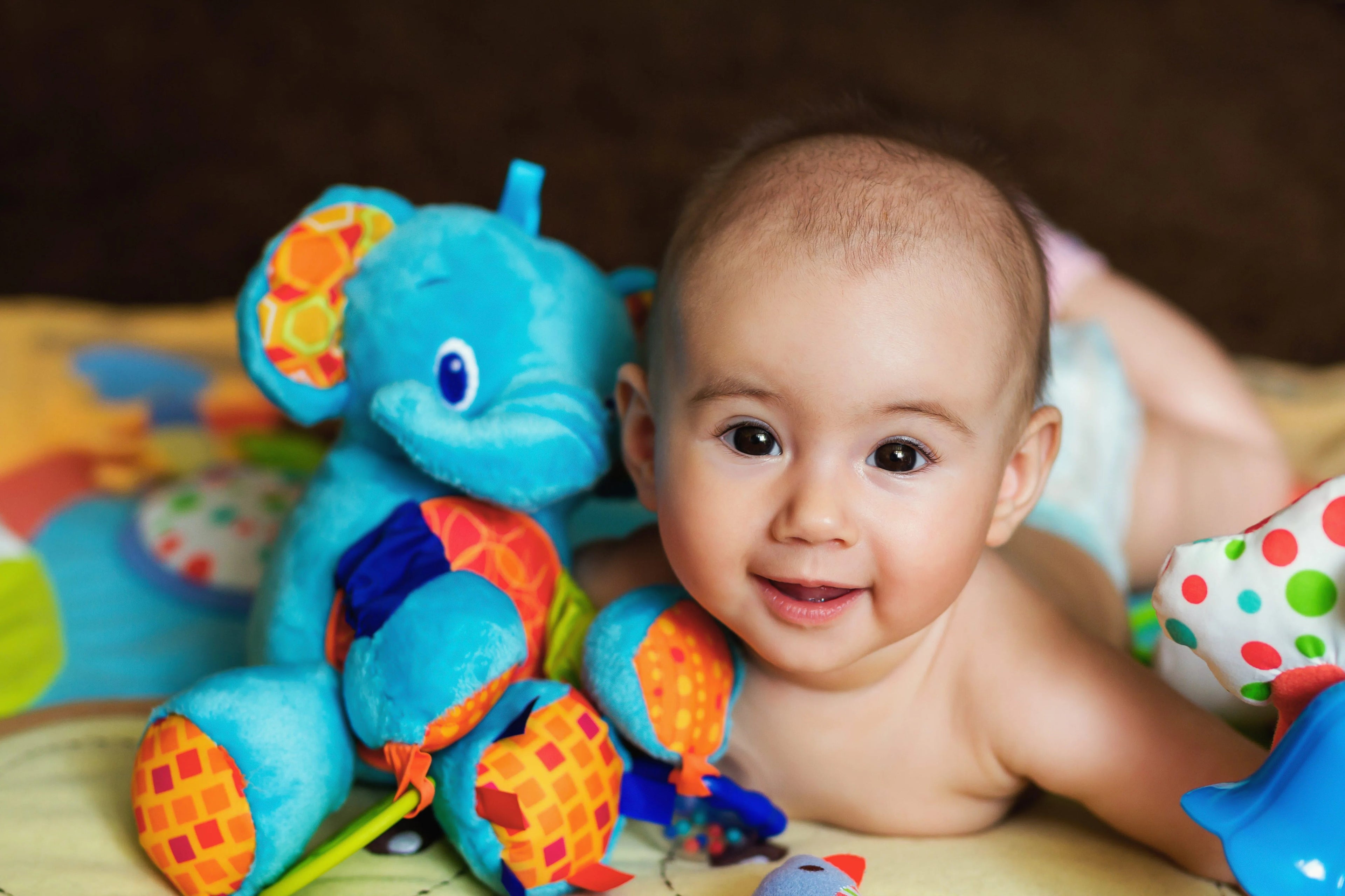 Baby lying on a play mat with colorful toys, including a blue elephant toy.